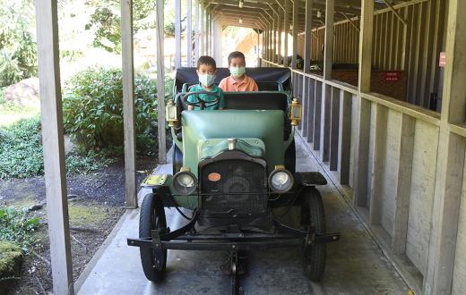 Two brothers drive an antique car in amusement park ride