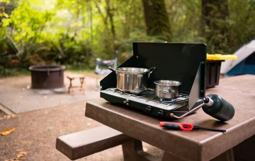 A Colman camp stove is seen on a picnic table at a wooded campsite best easy camping meals for families