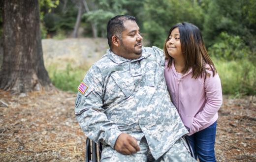 Veteran dad in army fatigues and sitting in wheelchair smiles at and hugs daughter of about age 11. she is smiling at him. veterans day events for families Seattle Bellevue Tacoma Puget Sound