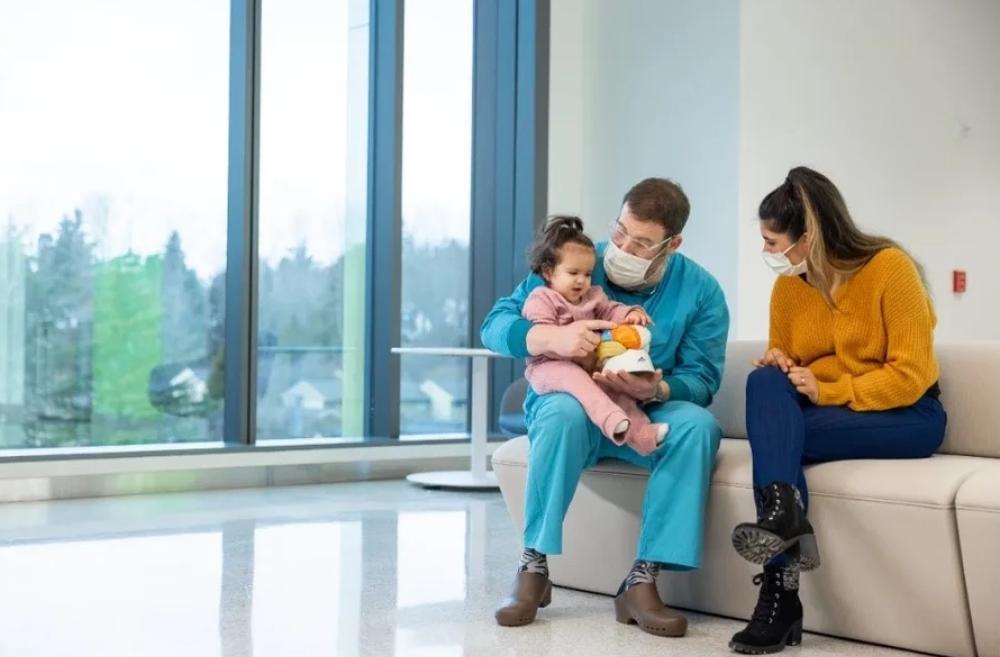 Young baby girl sitting in a doctor's lap with mom sitting next to them on a couch