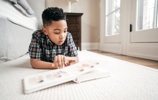 Young boy reads a book while lounging on the floor