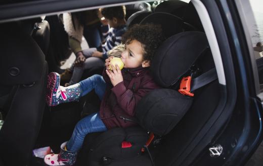little boy eating an apple in the back seat of a car