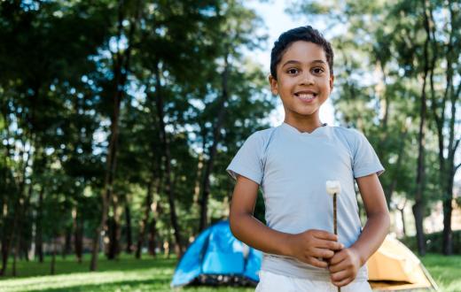 boy holding a marshmallow on a stick with two tents in the background
