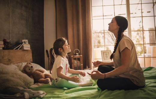 Mother and daughter practice meditation sitting on a bed