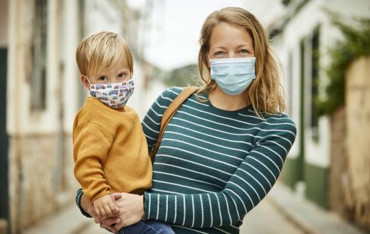 mother holding her son outdoors, both of them smiling under masks