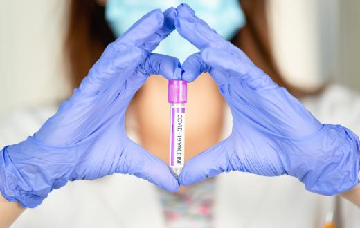 gloved hands making the shape of a heart around a vial with a covid vaccine label