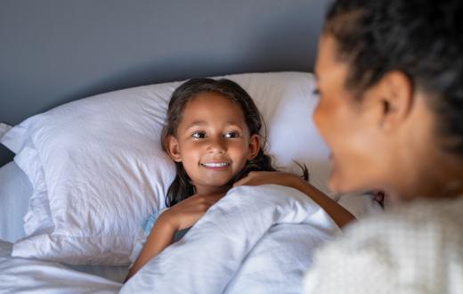mother sitting on the side of her daughter's bed with both smiling