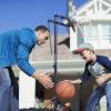 Father and son playing basketball outside of a big white house 