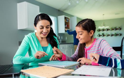 Mother helps her tween daughter with her homework at the kitchen table