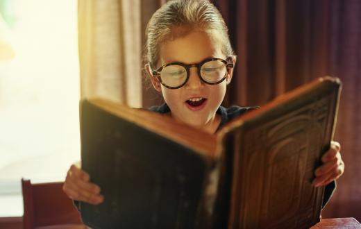 Young boy wearing glasses reads a magical book