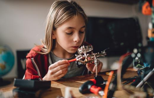 girl learning robotics in her room at home with robot parts on her desk