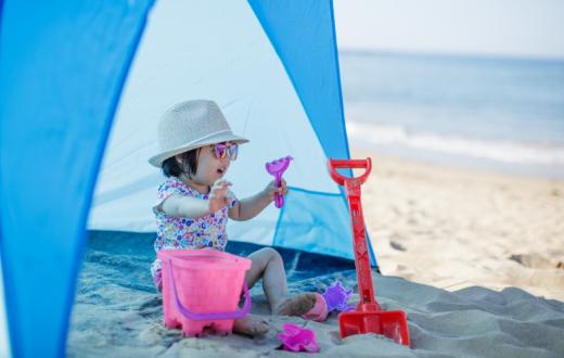Kid-wearing-sunhat-sitting-in-tent-by-the-beach