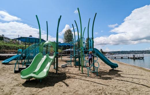 Child climbing on a blue and green play structure on the sand near the water