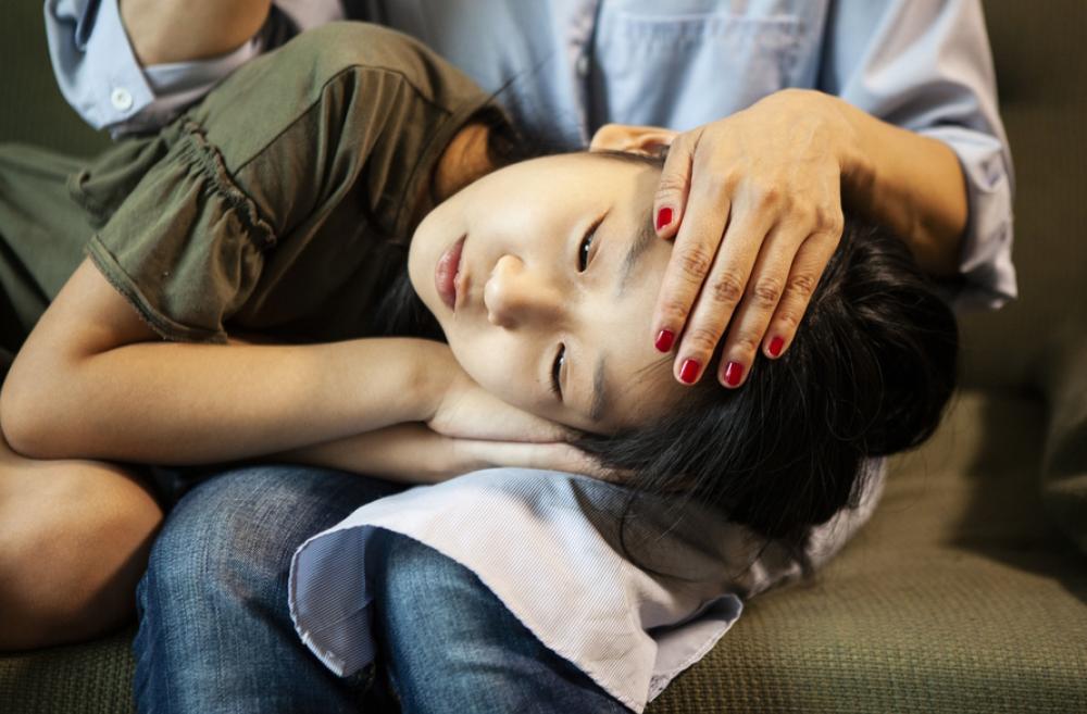 Young girl laying head in a parent's lap, feeling sick