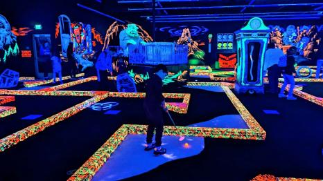 A boy plays mini golf on a blacklight course at Monster Mini Golf in Bellevue Washington new indoor family entertainment venue near Seattle fun for families
