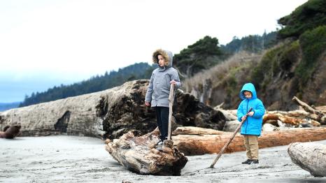 Boys in warm winter jackets standing on driftwood on a Pacific ocean beach on an off-season getaway to the Olympic peninsula