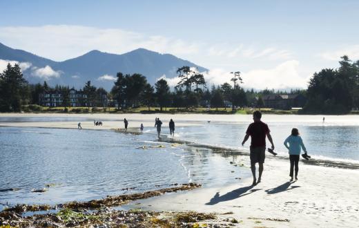A parent and child walk on a sand spit on the beach at Tofino, British Columbia, an amazing road-trip destination for families from Seattle