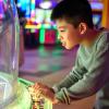 A tween-age boy about 11 plays an arcade game on a independence-building outing with friends around Seattle