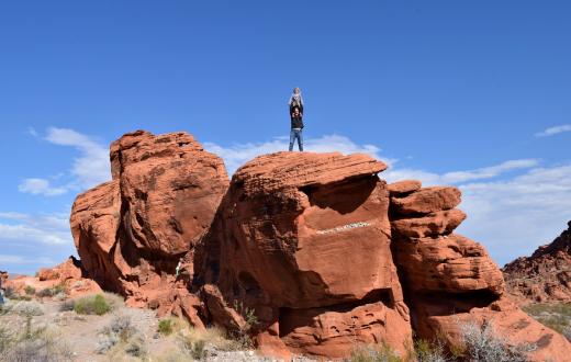 father with a kid on his shoulders standing on top of a tall red rock in the valley of fire